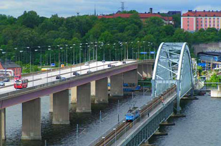 Alla som ska ta sig till Lidingö på hjul, med bil, buss, tåg, cykel eller genom att gå, måste göra det på någon av de två Lidingöbroarna. Den stora, till vänster, invigdes 1971 och den låga "Gamla Lidingöbron" till höger, invigdes 1925. Längst till höger skymtar Ropstens tunnelbanestation och i bakgrunden syns Hjorthagen i Stockholm. En ny bro, "Lilla Lidingöbron", som ersätter Gamla Lidingöbron, ska vara klar i september 2023.