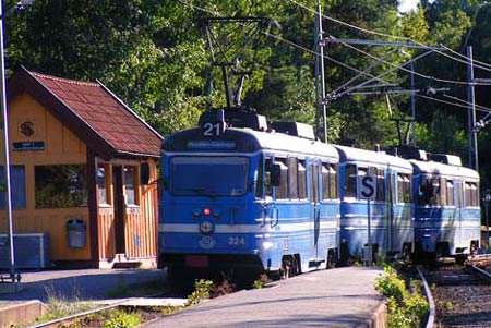 Lidingötåget lämnar Högberga stations stickspår för att åka på enkelspår till Kottla och Skärsätra. Stationsbyggnaden är den ursprungliga.